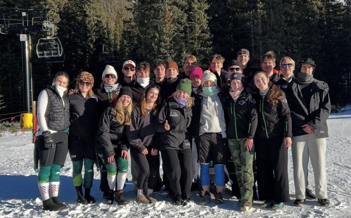 Plymouth State University ski team in front of a white wall in green skiing racing suits